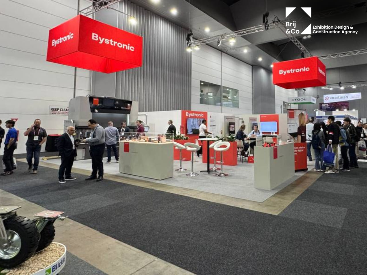 Bystronic exhibition stand with red hanging signs and white meeting tables