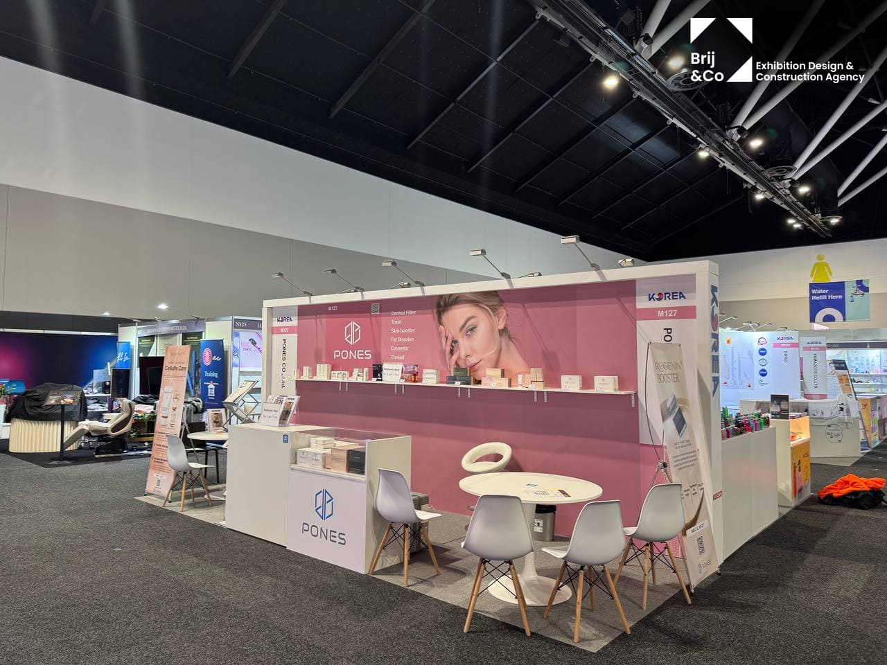 Exhibition stand with a pink backwall, white tables and chairs