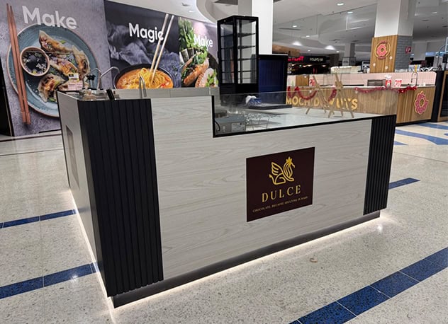 Dulce kiosk counter with dark vertical panels and a lit base