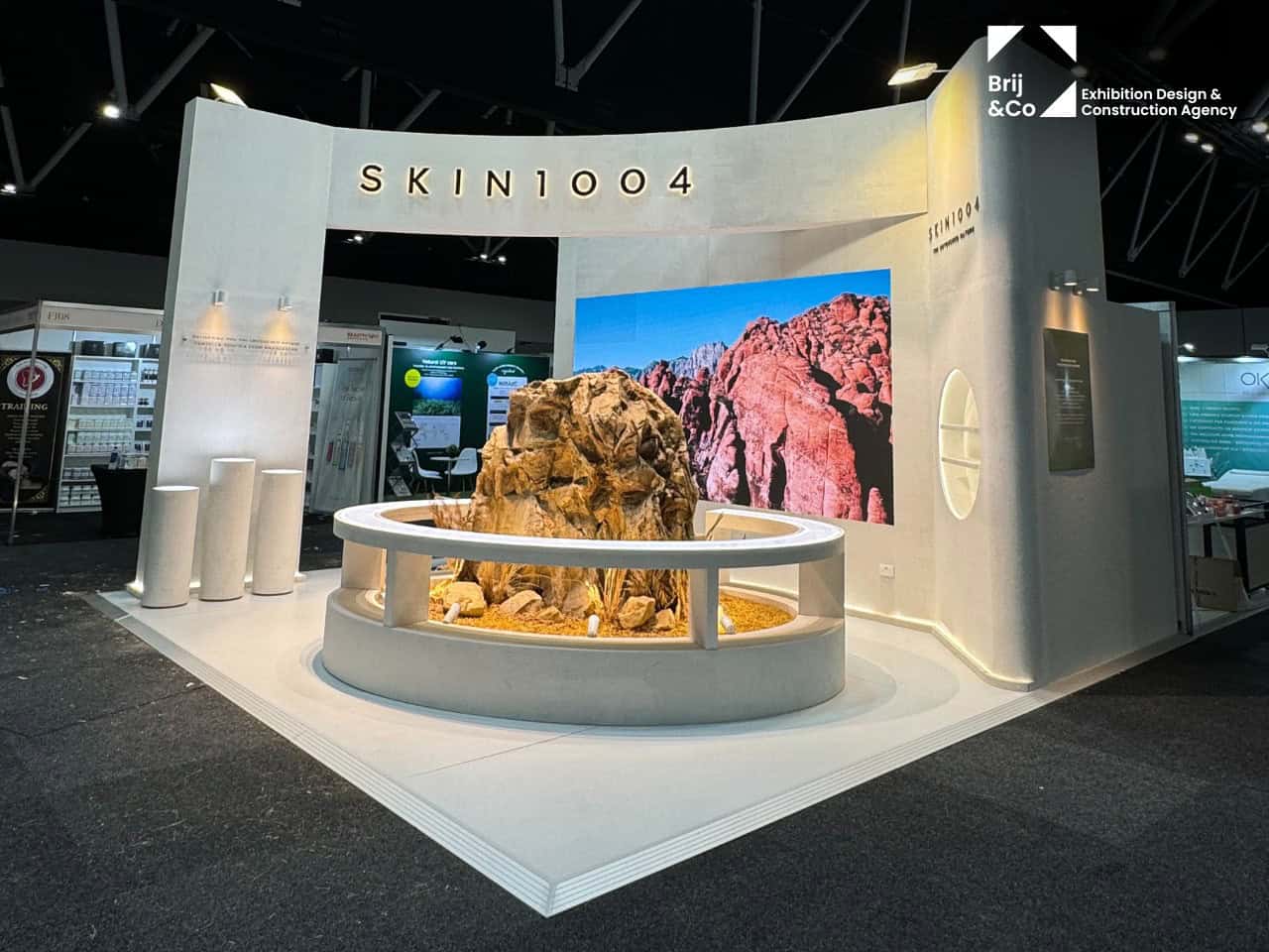 SKIN1004 exhibition stand with a curved white wall and a desert-scene screen