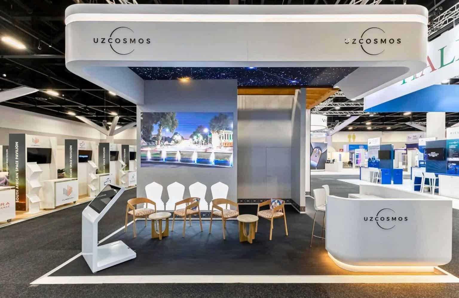 Uzcosmos exhibition stand with a white canopy, screen and seating area