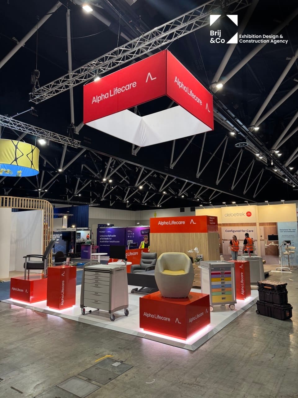 Alpha LifeCare exhibition stand with a red hanging banner, chairs and display plinths