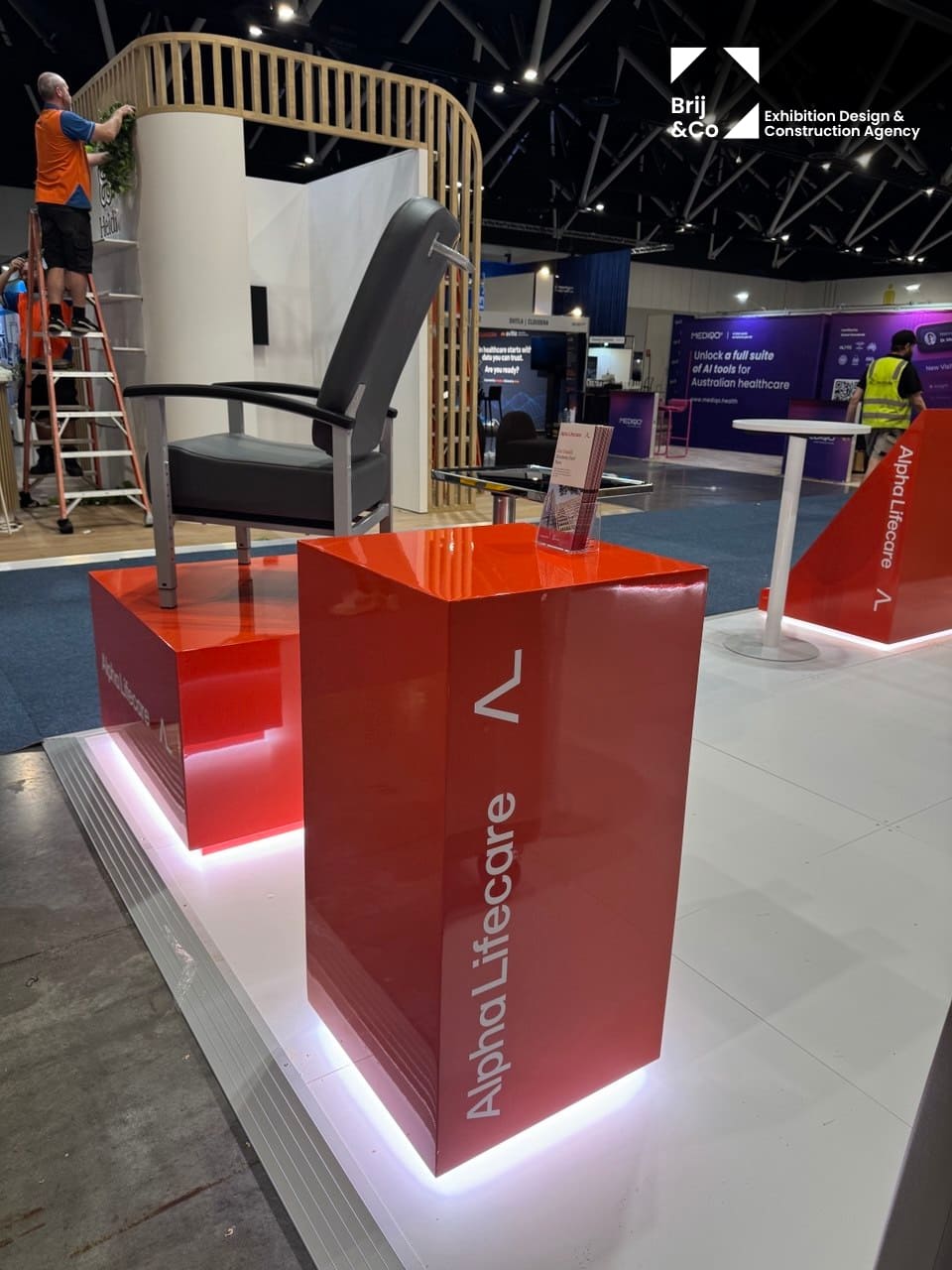 Alpha LifeCare branded red display plinth with a chair on a white stand floor