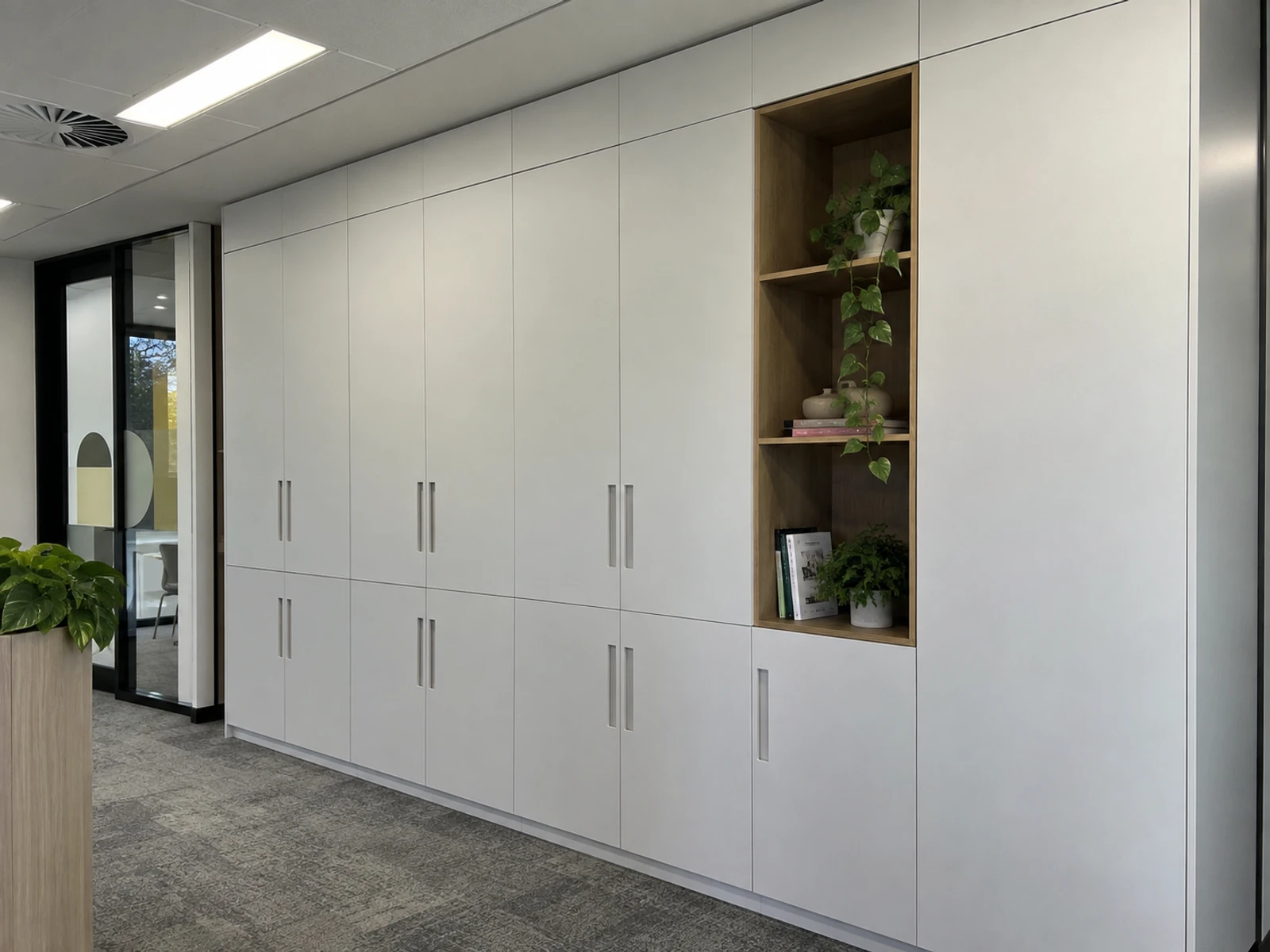 Floor-to-ceiling office storage wall with white laminate doors and an open timber niche